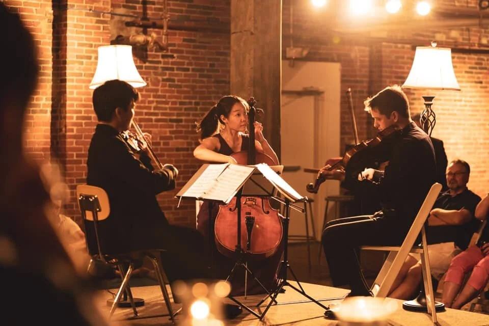 A string quartet plays by lamplight against brick at a VIVO concert
